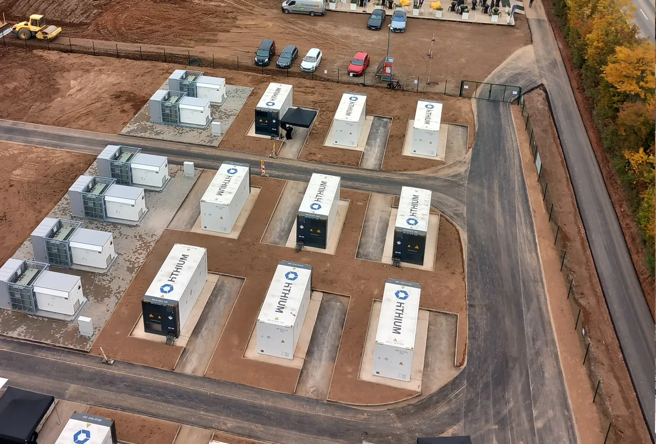 Foto aerea reale di un cantiere di accumulo: container di batterie su fondazioni appena realizzate, accanto terreno livellato e strada di accesso